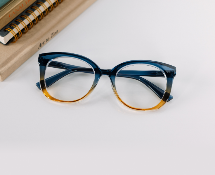 Blue and gold eyeglasses on a white surface with a notebook in the background